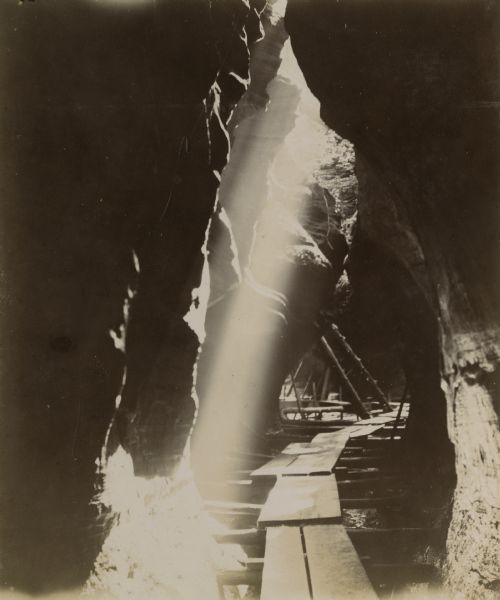 A beam of sunlight falls down into a shaded crevice towards a boardwalk.