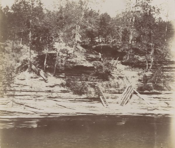 View of rock formations along the Wisconsin River. Several sets of wooden stairs are built into the landforms and lead down to the river.