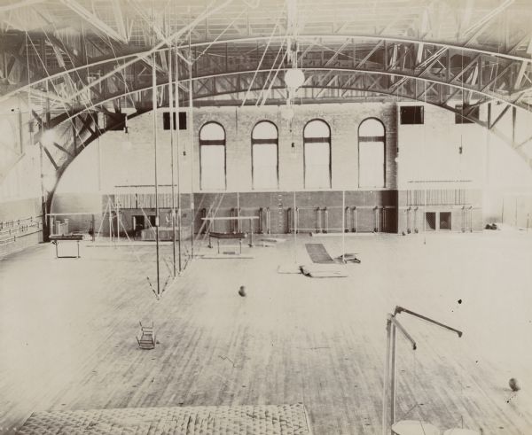 Elevated interior view of the University of Wisconsin-Madison Red Gym (Old Red or Armory) main floor. Gymnastic equipment is set up throughout the large, wooden-floored space.