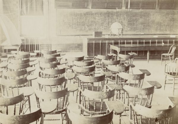 View of an empty University of Wisconsin-Madison lecture room filled with rows of chairs. A globe and blackboard are visible at the front of lecture hall.