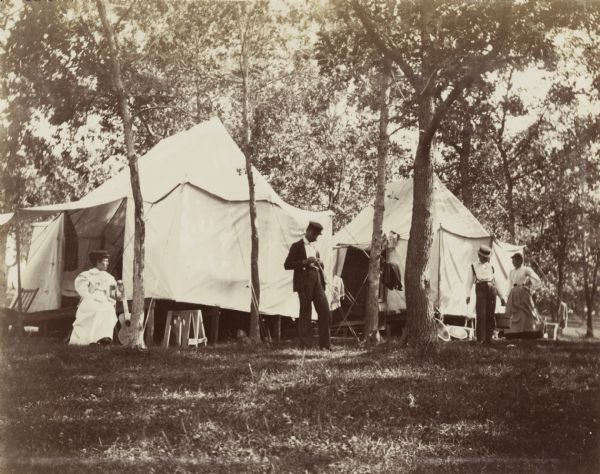 The Jonas' campsite at Merrill Springs. There are two tents pitched in a grove of trees. Two women and two men are outside the tents.