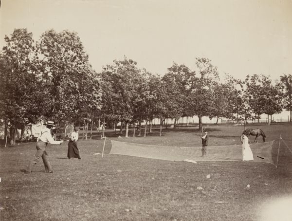 Four individuals, presumably the Jonas family, play badminton at their campsite. A horse grazes behind the individuals playing badminton.