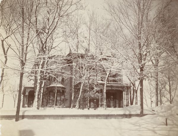 Exterior view of a large house in the wintertime. The house has Italianate details such as decorative brackets and balustrades, and a low-angle roof.