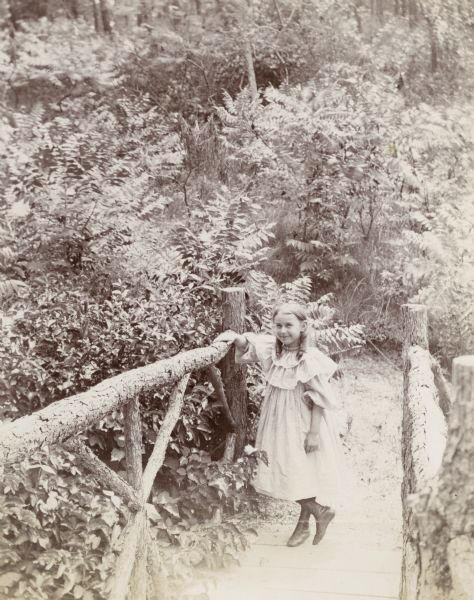 A young girl poses on a rustic wooden bridge in the woods.
