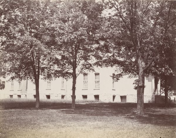 Exterior view of the main building at the Wisconsin School for the Deaf. The building is surrounded by a lawn and a grove of trees.