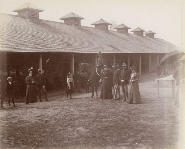 Women and children visit soldiers at Camp Harvey. A long building with other people on a long porch is in the background.
