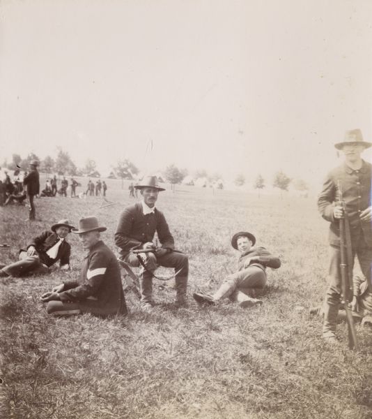 Soldiers resting on the grass at Camp Douglas. In the background are tents pitched among trees.