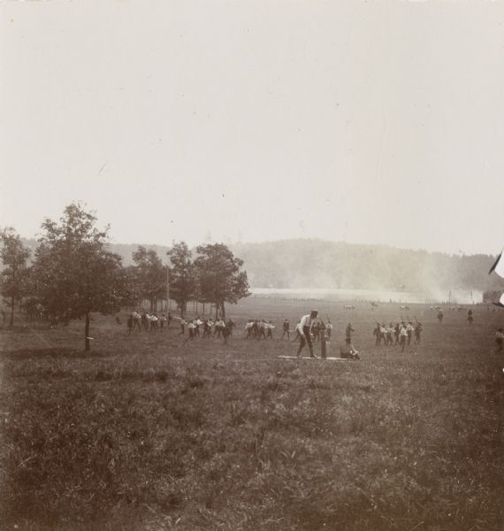 View down hill of the 3rd Regiment enacting a mock battle in an open, rural area.