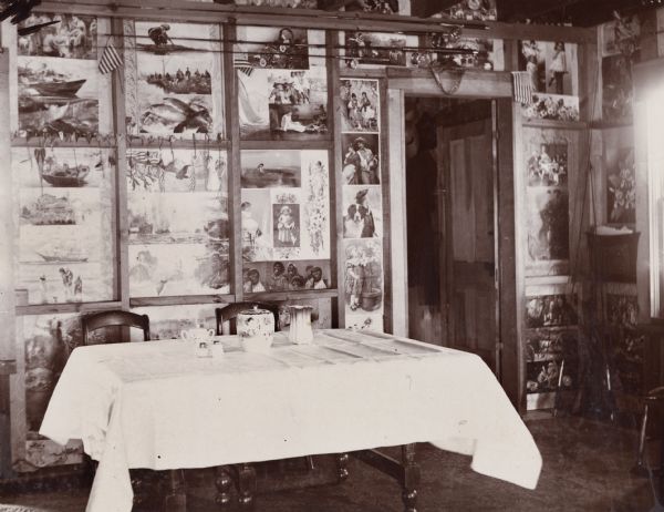 An interior view of U.S. Marshall Canon's summer cottage. Behind a table, a wall is decorated from floor to ceiling with photographs and other artwork, as well as fishing poles and fish hooks.