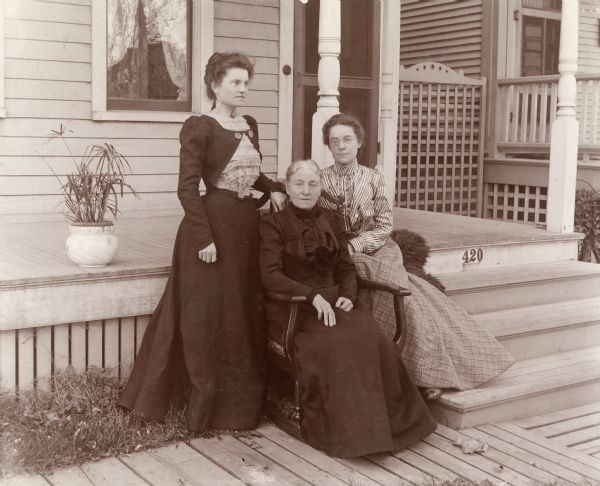 Three women, from left to right: Mrs. Lucy, Mrs. Theresa and Mrs. Cosgrove. They are posing near a front porch.