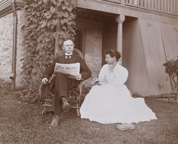 Mr. and Mrs. Zimmerman sitting outside their house relaxing in the yard. Mr. Zimmerman reads "The State" paper, and Mrs. Zimmerman has flowers in her hand.