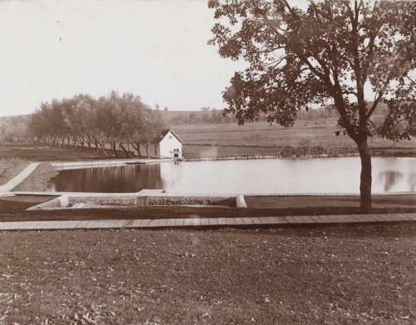 A landscape view of the Wisconsin State Fish Hatchery (aka Nevin Fish Hatchery, 3911 Fish Hatchery Rd) grounds. A large reservoir is visible with a small outbuilding at its shore.