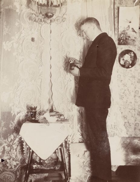 An unidentified man stands near a lace-curtained window in a Victorian-era home. The photograph's corresponding caption reads, "Flash light."