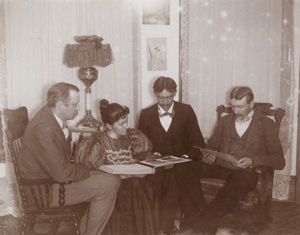 Four Schildhauers: H., Annie, Rudolph and Edward, sit in a parlor and look at a photo album.