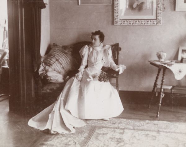 Mrs. D.W. Osborn sits on a loveseat in a Victorian-era home. She sits in her wedding dress with a bouquet of flowers on her lap.