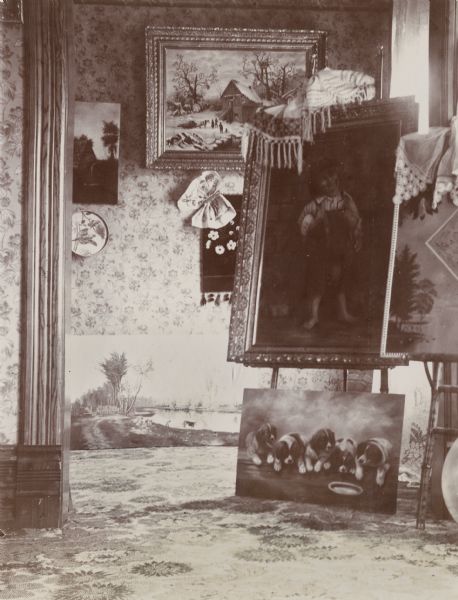View of a Victorian-style room in the H. Schildhauer residence at 13 North Webster Street. Various paintings are on display in the room, some on easels, others leaning or displayed against the far wall.