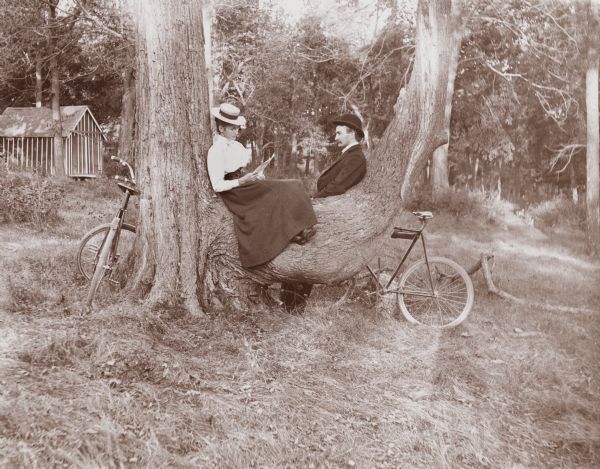 Mrs. H. and Edward Schildhauer rest on a large tree limb near lake Mendota. They are, presumably, resting from a bike ride along Mendota Drive.
