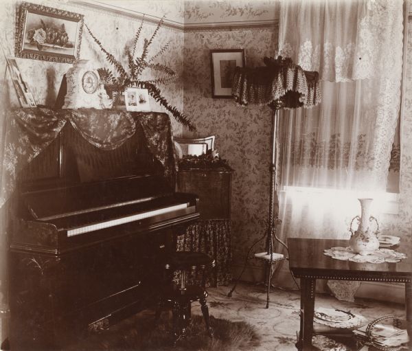 View of a piano and surrounding furniture in the Victorian-era home of Harry G. Potter. Potter lived on North Gorham Street and was, according to a caption on the original print, a "Dep. Col. in the Revenue Office."