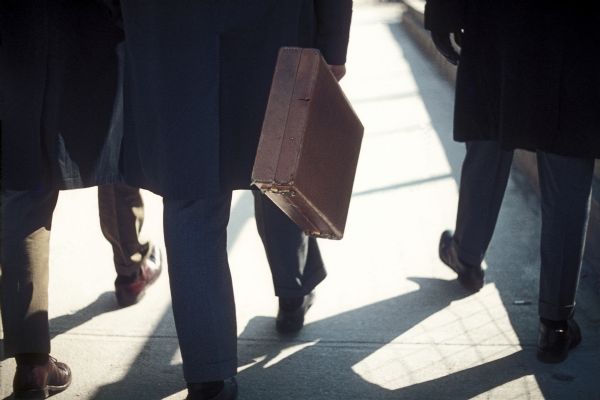 Close-up view of a man with a briefcase as he walks on the sidewalk by the construction of the World Trade Center towers.