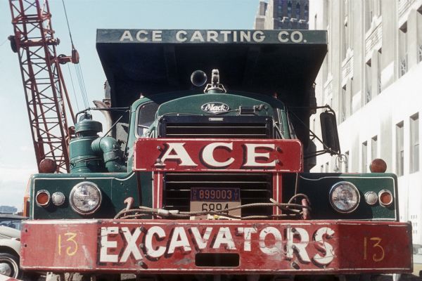 Color photograph of an Ace Carting Company truck with "Ace Excavators" on the front. The truck is on the site of the construction of the World Trade Center towers.