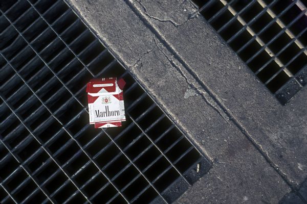 A pack of Marlboro cigarettes lays atop a sewer grate on a city street.
