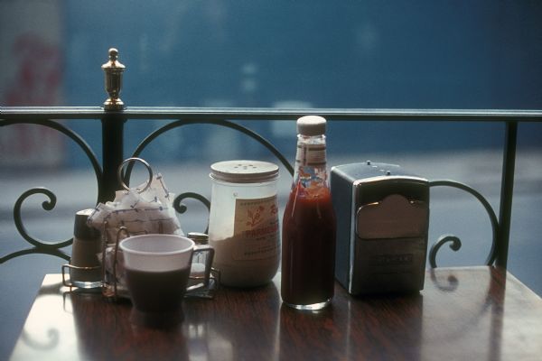 Various condiments sit atop a table near a decorative railing at what appears to be a restaurant.
