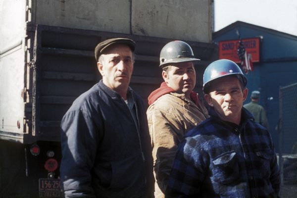 Three construction workers standing near a truck outside the office for the Sand Chapter of Mechanical Contractors at the construction site for the World Trade Center.