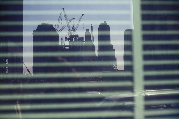 View of the construction process of the World Trade Center through a window with venetian blinds.
