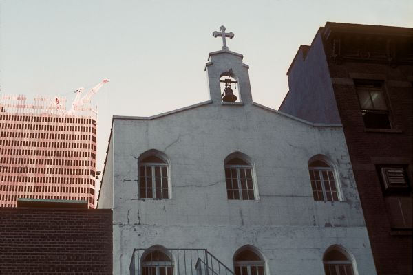A church with a bell tower is in the foreground. The framework of one of the towers of the World Trade Center is in the background.