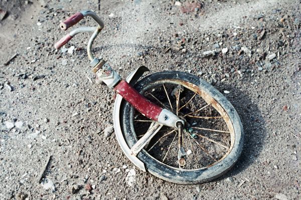 The front wheel and handlebars of a tricycle lays in the dirt.