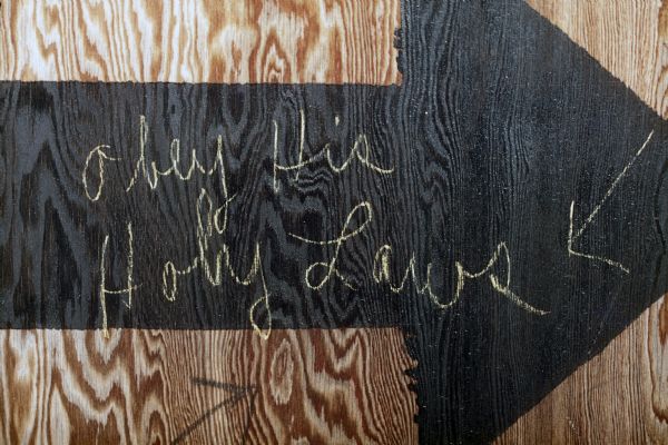 A painted arrow on plywood has writing that reads, "Obey His Holy Laws."