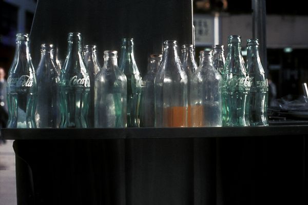 A group of Coca-Cola and other glass bottles are gathered in a tray on top of a table.