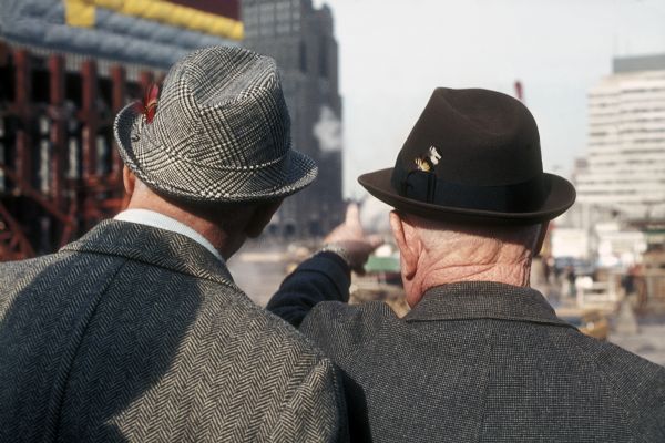Rear view of two men in suits and hats viewing the progress of the construction of one of the World Trade Center towers.