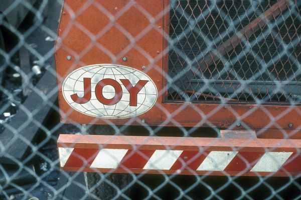 View through chain link fence of a logo that says: "Joy" on a piece of construction equipment.