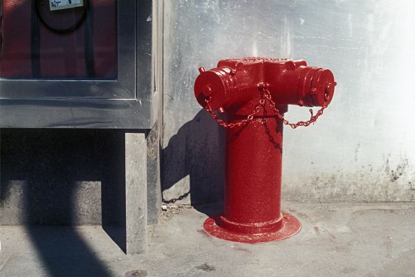 View of a red hydrant on a sidewalk next to a wall.