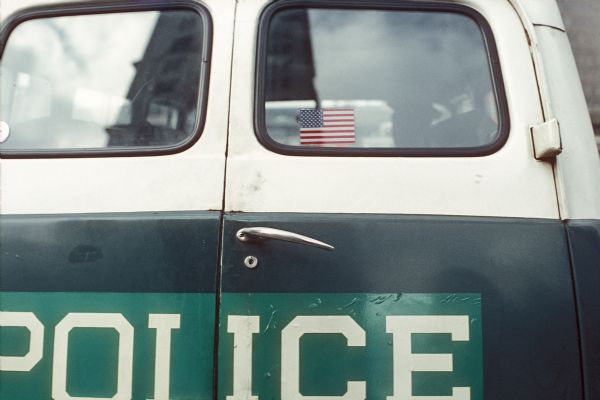 View of the doors of the back of a police vehicle. An American flag sticker is visible in the window.