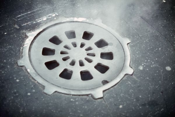 A manhole cover in the street with steam coming through its openings.