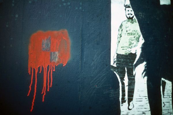 A drawing of a man on the side of a building, perhaps the remains of a poster. On the left is an orange spray painted area.