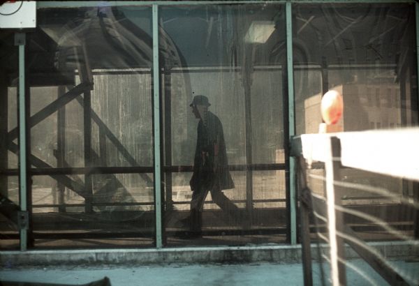 A man walks through the construction for the World Trade Center. A reflection of the surrounding buildings is visible in the windows.