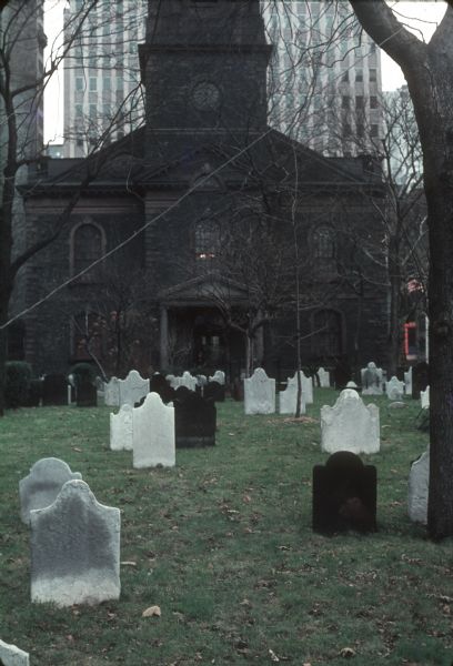 View of cemetery of St. Paul's Chapel with gravestones. In the background is the construction of the World Trade Center.