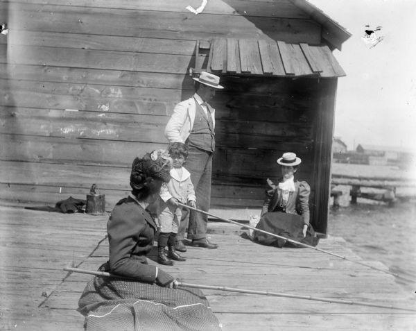 Syl with two women and a man, all wearing hats, fishing off of a dock in Sturgeon Bay. Behind them is a small wooden structure.