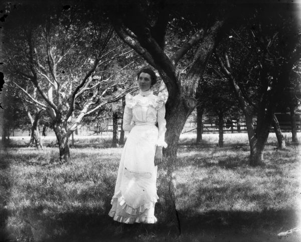 Aunt Helen posing against a tree wearing a dress in an orchard.