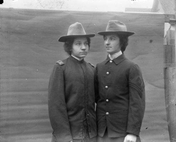 Aunt Helen and Mrs. Quill stand shoulder to shoulder in front of a backdrop. They are both wearing military style uniforms including hats.
