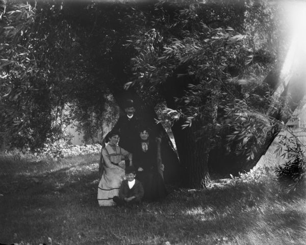 Syl, his "Mama" Annette, aunt Helen and Will posing on and around a rustic bench under a willow tree.
