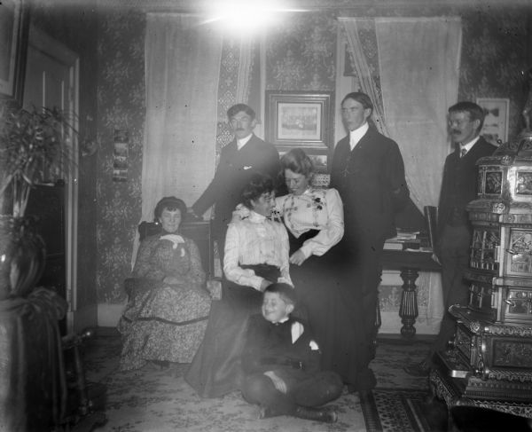 Mr. and Mrs. Perry posing in the Dankoler house. Syl is seated on the floor in front of them, and Harry stands on the far right near a cast iron stove.