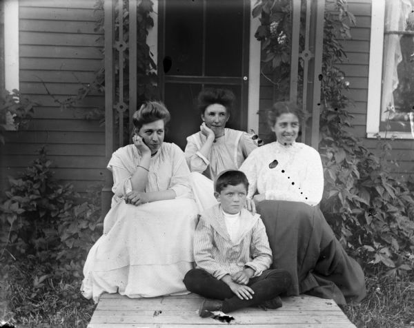 Three women in long dresses sit on the front stoop of a house with Syl.