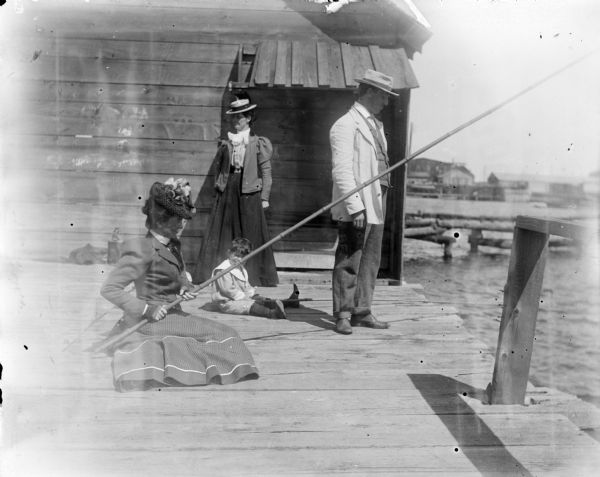 A young Syl fishing with three other adults off a pier using cane poles.