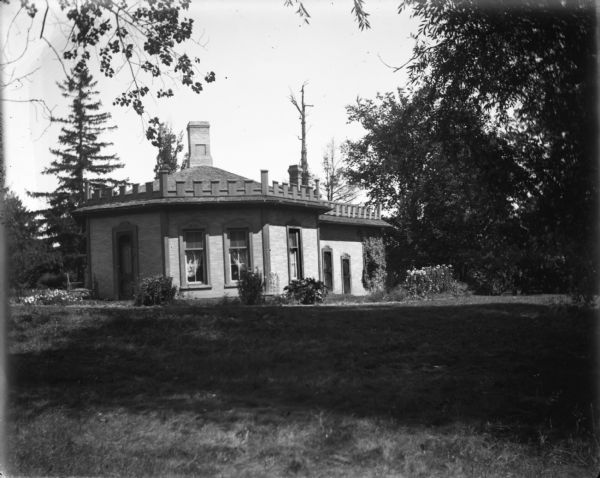 An exterior view of Octagon Cottage. The edge of the roof has crenelations along it, and a brick chimney is in the middle the roof.