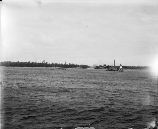 View across water of Sturgeon Bay. In the far distance are lighthouses, buildings, and barges along the shoreline.