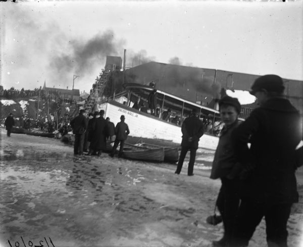 A crowd gathers at Milwaukee Harbor standing on ice around the <i>Julius Goll Jr.</i> excursion boat.